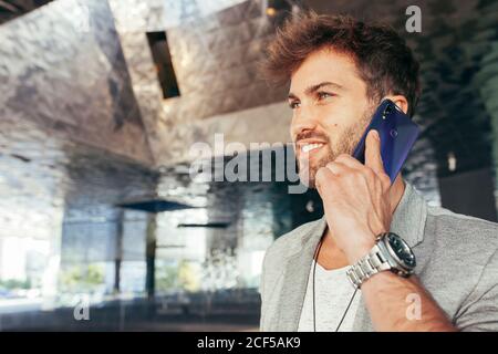Handsome young male entrepreneur in casual clothing calling on mobile phone and looking away at modern underground car park Stock Photo