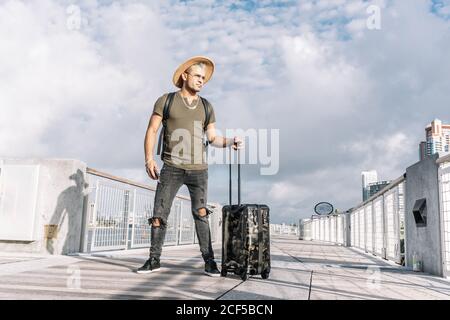 Traveler man with a hat walking with suitcase in the street. Travel concept. Stock Photo