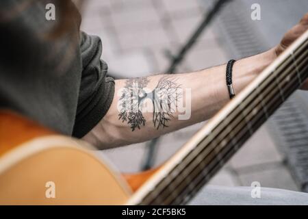 Close-up view of tattoo on arm of anonymous street musician playing a classic acoustic guitar