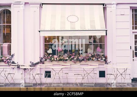 Facade of empty terrace of modern cafe with pink wall and window decorated with flowers and hearts on city street Stock Photo