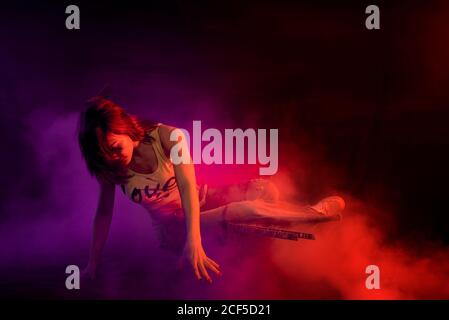 Modern female performing break dance on floor in purple and red smoke on black background Stock Photo