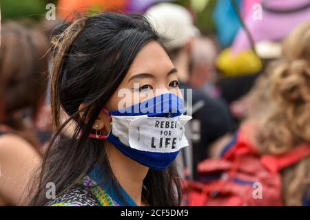 A protester with a facemask saying ‘Rebel for Life’ during the demonstration.Outside the HM Treasury buildings Protesters at the Extinction Rebellion Carnival of Corruption marched towards Buckingham Palace but were blocked by police at The Mall. Activists demand for those in power to take action on climate and environment issues. Stock Photo
