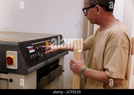 Low angle of woodworker setting up special planning electric machine before using while working with timber in light modern workroom Stock Photo