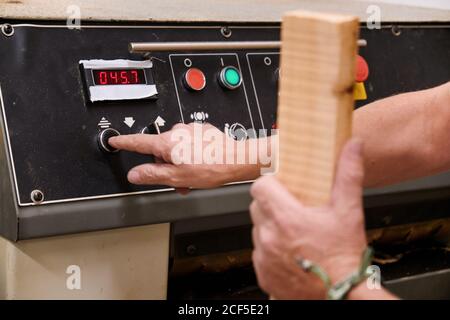 Low angle of unrecognizable woodworker setting up special planning electric machine before using while working with timber in light modern workroom Stock Photo