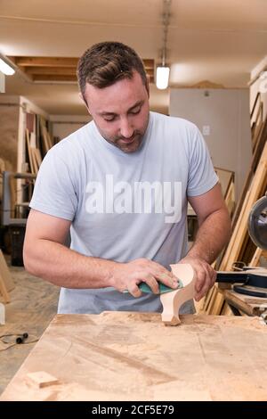 Artisan polishing wooden detail using sandpaper in carpentry workshop Stock Photo