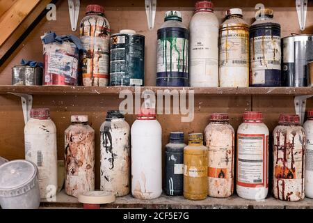 Collection of plastic and metal multicolored bottles and jars of special chemicals for carpentry work on wooden shelves in contemporary workroom Stock Photo