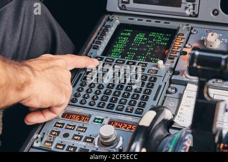Crop anonymous male pilot using keyboard of flight management system in cockpit of modern aircraft during flight Stock Photo