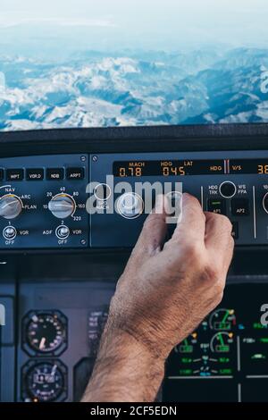 Back view of crop anonymous male pilot turning switch on control panel in cockpit during flight over rocky terrain Stock Photo