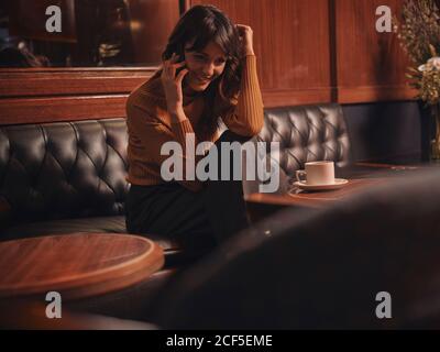 Stylish cheerful Woman talking on mobile phone comfortably sitting at round table in cafe Stock Photo