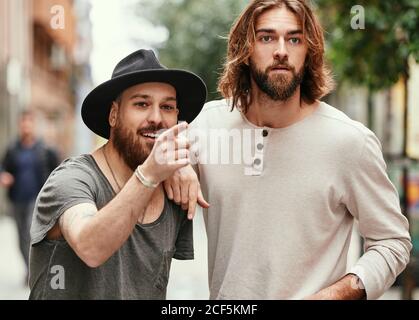 Handsome man in black hat pointing to friend looking with interest in street Stock Photo
