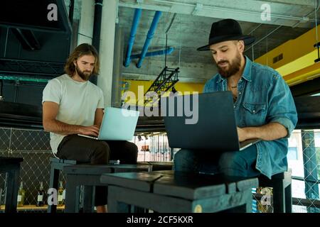 Young handsome bearded men seriously and concentrated working typing on notebooks on knees Stock Photo
