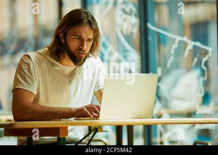 Young bearded handsome man sitting in outside cafe and working holding notebook on table Stock Photo