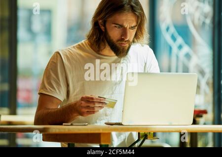 Young bearded handsome man sitting in outside cafe and working holding notebook on table Stock Photo
