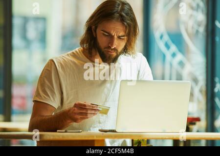 Young bearded handsome man sitting in outside cafe and working holding notebook on table Stock Photo