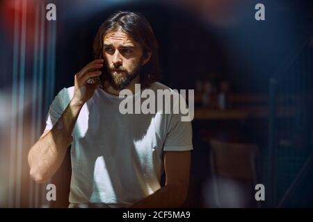 Young bearded handsome man in cafe behind window talking on phone Stock Photo