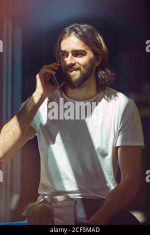 Young cheerful bearded handsome man in cafe behind window talking on phone Stock Photo