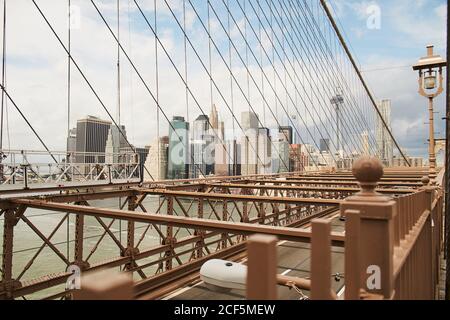 Contemporary skyscrapers of New York City seen through cables of Brooklyn Bridge against blue cloudy sky Stock Photo