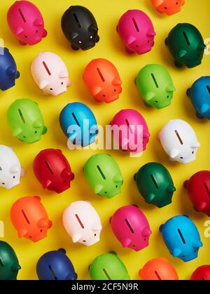 Top view of bright multicolored piggy banks arranged in pattern on yellow background Stock Photo