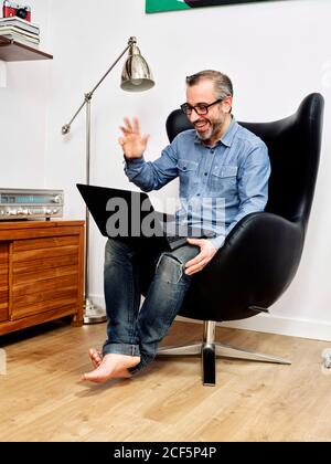 man working on laptop and talking on video conference smiling having relaxed coffee on couch at home Stock Photo