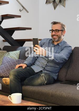 man talking smiling on the video conference at phone from the sofa at home Stock Photo