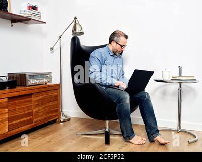 man working on laptop having a relaxed coffee on the armchair at home Stock Photo