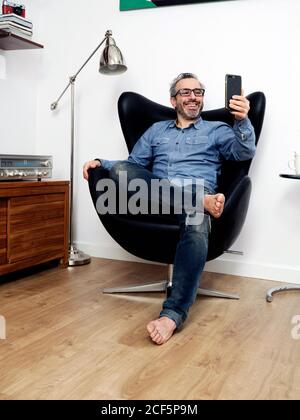 man taking a selfie smiling having a relaxed coffee on the couch at home Stock Photo