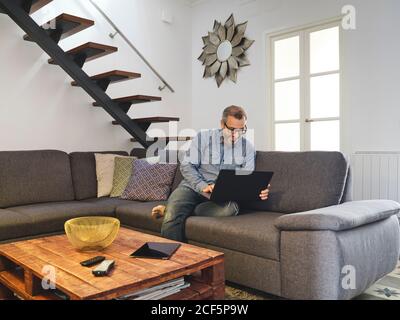 man working on laptop alone on sofa in living room at home Stock Photo