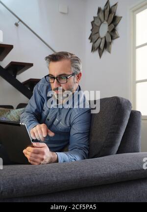 man using tablet surfing the internet alone on the couch in the living room at home Stock Photo
