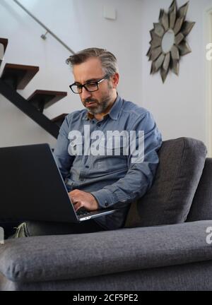 Serious man using laptop surfing the internet alone on the couch in the living room at home Stock Photo