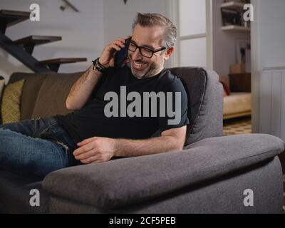 Relaxed man talking on the phone smiling alone on the sofa in the living room at home Stock Photo