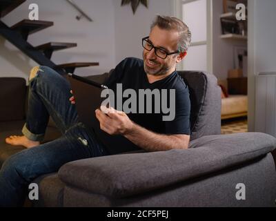 Relaxed man talking on the tablet serious alone on the sofa in the living room at home Stock Photo