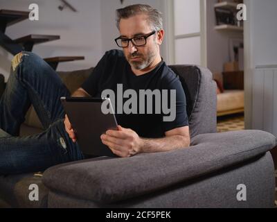Relaxed man talking on the tablet serious alone on the sofa in the living room at home Stock Photo