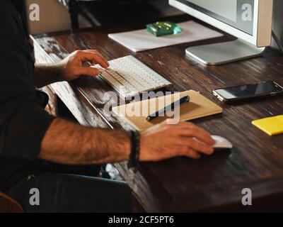 detail of man hands working at home desk with computer via internet typing on computer and using mouse Stock Photo