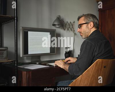 man working at home desk with computer via internet typing on computer and using mouse Stock Photo