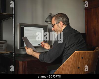 man working at home desk with computer via internet reviewing bills and reports Stock Photo