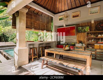 Cozy dining place on villa with counter and wooden table served with bowl of various exotic fruits on sunny day Stock Photo