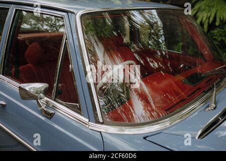 Vintage car with red antique interior parked under tropical trees reflected in windshield Stock Photo