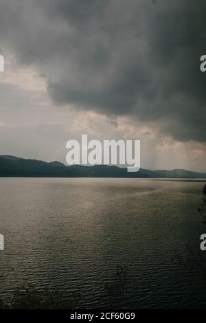 Tranquil landscape with sun rays shining through thick clouds over calm lake with dark water Stock Photo