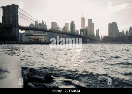 Amazing low angle cityscape of New York City with Brooklyn Bridge over river and skyscrapers in sunlight at sunset time Stock Photo