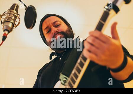 Adult man in music studio playing a guitar and singing in a microphone Stock Photo