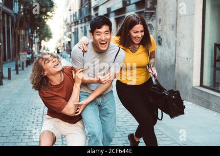 Smiling multiethnic people in casual clothes playing while strolling along urban street Stock Photo