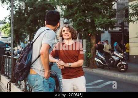Carefree interested multiethnic men in casual clothes talking while standing city street Stock Photo