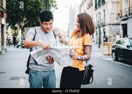 Positive laughing multiethnic people looking for direction on map while standing on city street Stock Photo