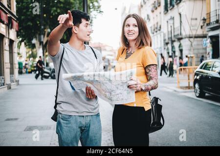 Positive laughing multiethnic people looking for direction on map while standing on city street Stock Photo