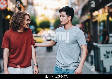 Carefree interested multiethnic men in casual clothes talking while strolling along city street Stock Photo