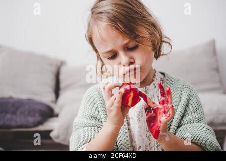 Funny child with hands in colors painting Easter egg near sofa on blurred background Stock Photo