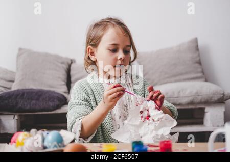 girl with brush coloring chicken eggs at table in room Stock Photo