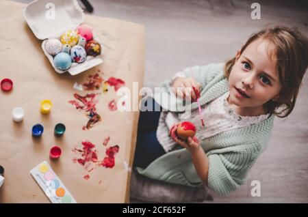 girl with brush coloring chicken eggs at table in room Stock Photo