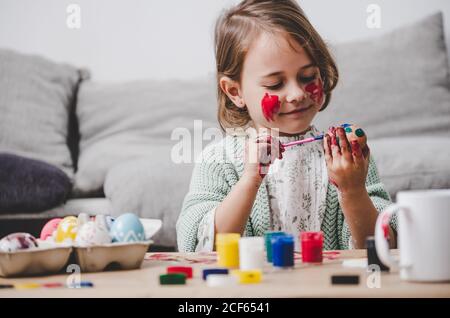 girl with brush coloring chicken eggs at table in room Stock Photo