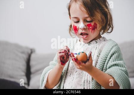 girl with brush coloring chicken eggs at table in room Stock Photo